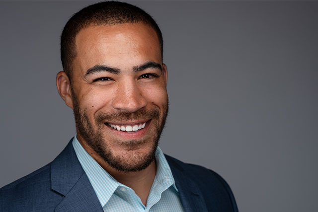 middle aged light tone black man, professional, in suit with open collar smiling for professional headshot photo.