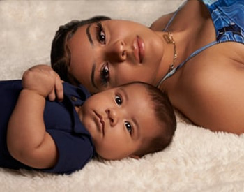 A woman and a baby lie next to each other on a soft, white surface, looking towards the camera.